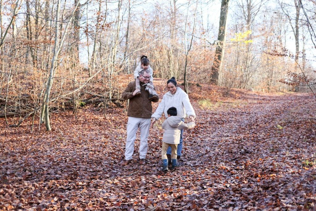 Parents et enfants en balade sur un chemin de forêt couvert de feuilles en automne